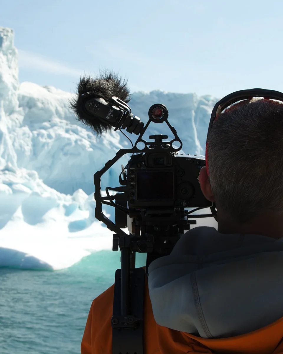 Filming an iceberg from a boat in Greenland, the camera operator seen from behind