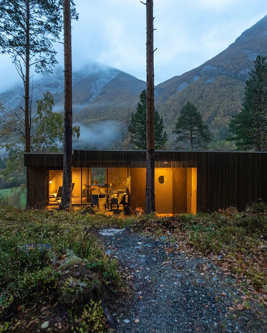 Dark timber cabin with lit windows in a mountain forest