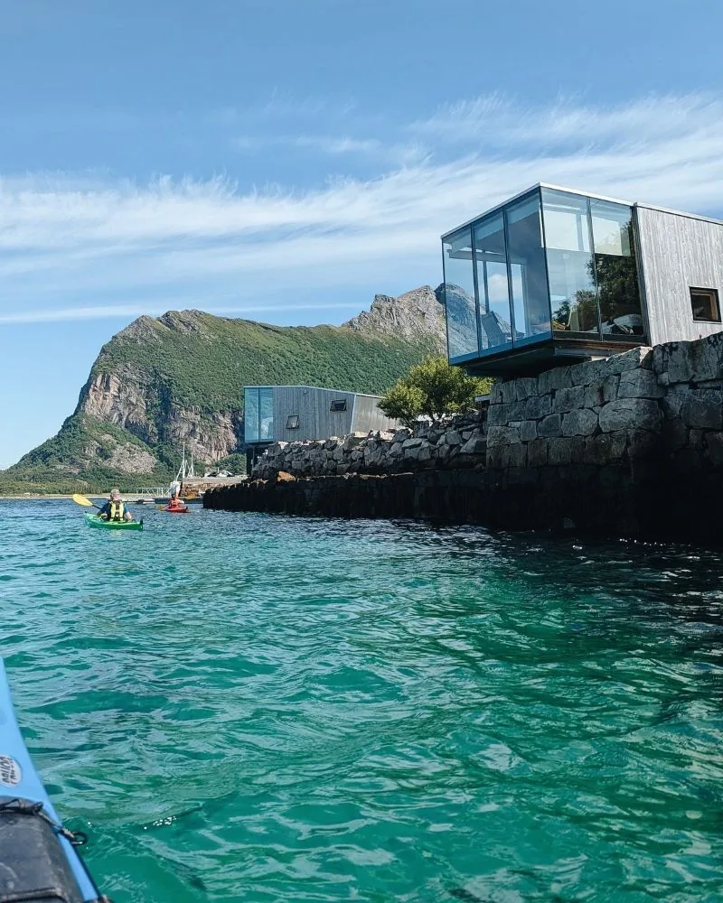 Kayak passing glass-fronted cabins on the rocks