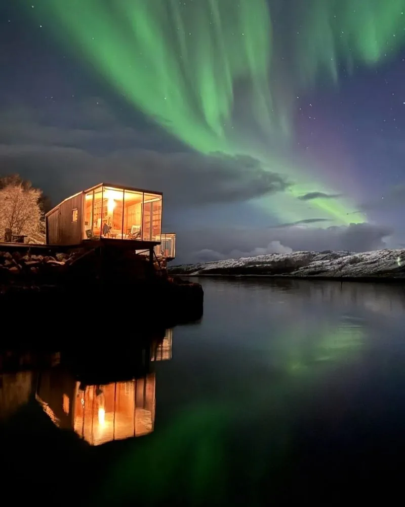 Lit cabin by the water under the northern lights