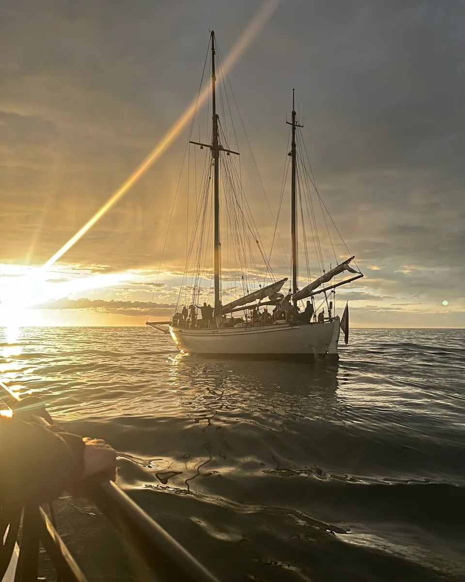 Two-masted wooden schooner at sunset with guests on deck