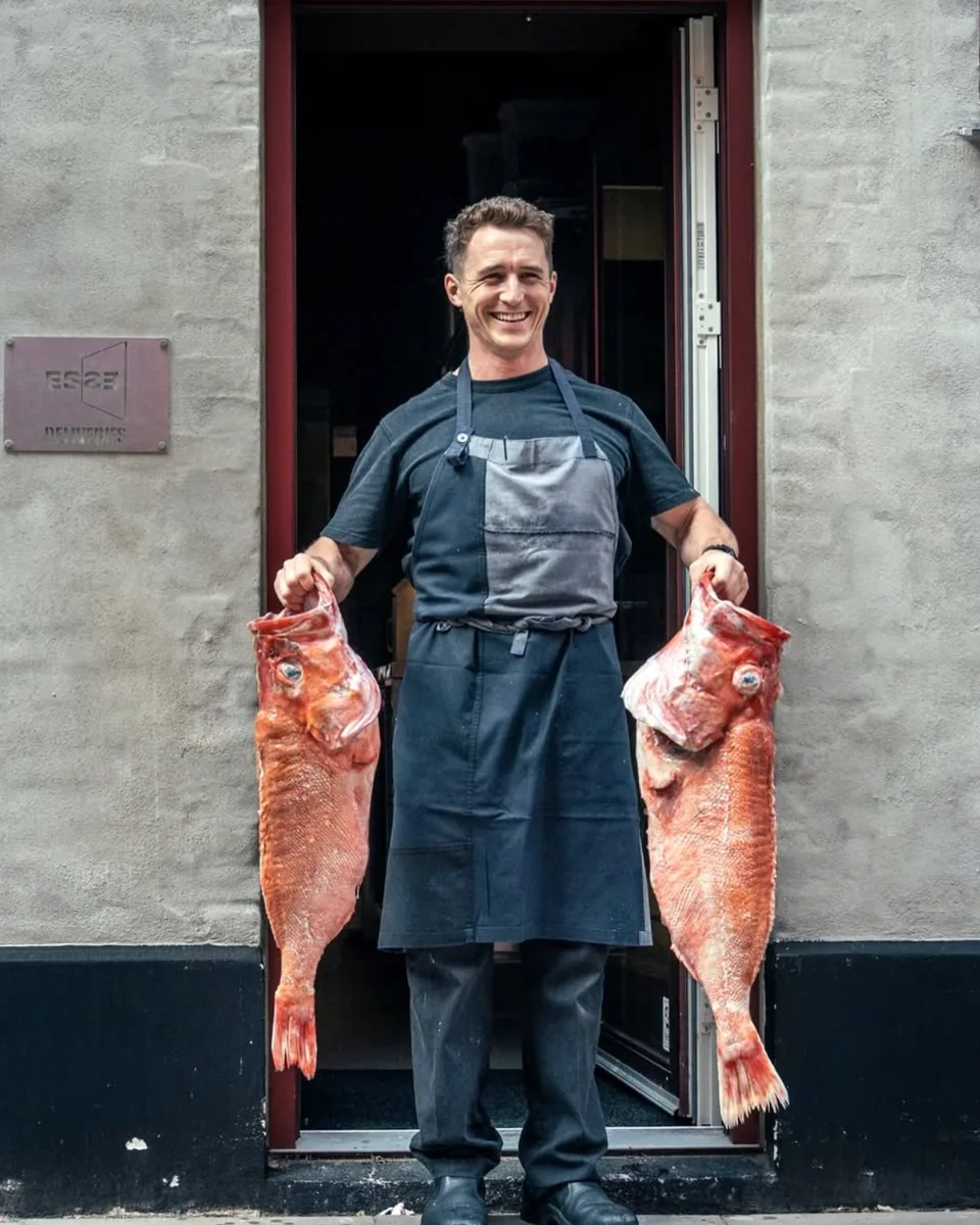 A chef in an apron holding two large redfish outside a restaurant door