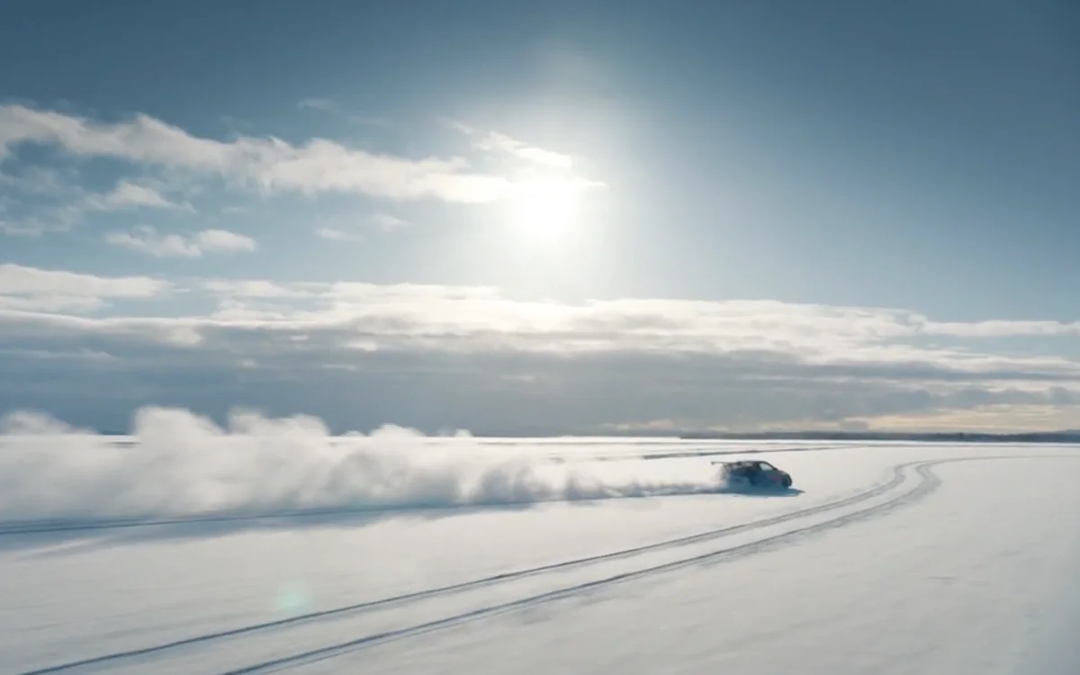 En bil, der driver hen over en frossen sø i lav sol, med sneen sprøjtende bag sig