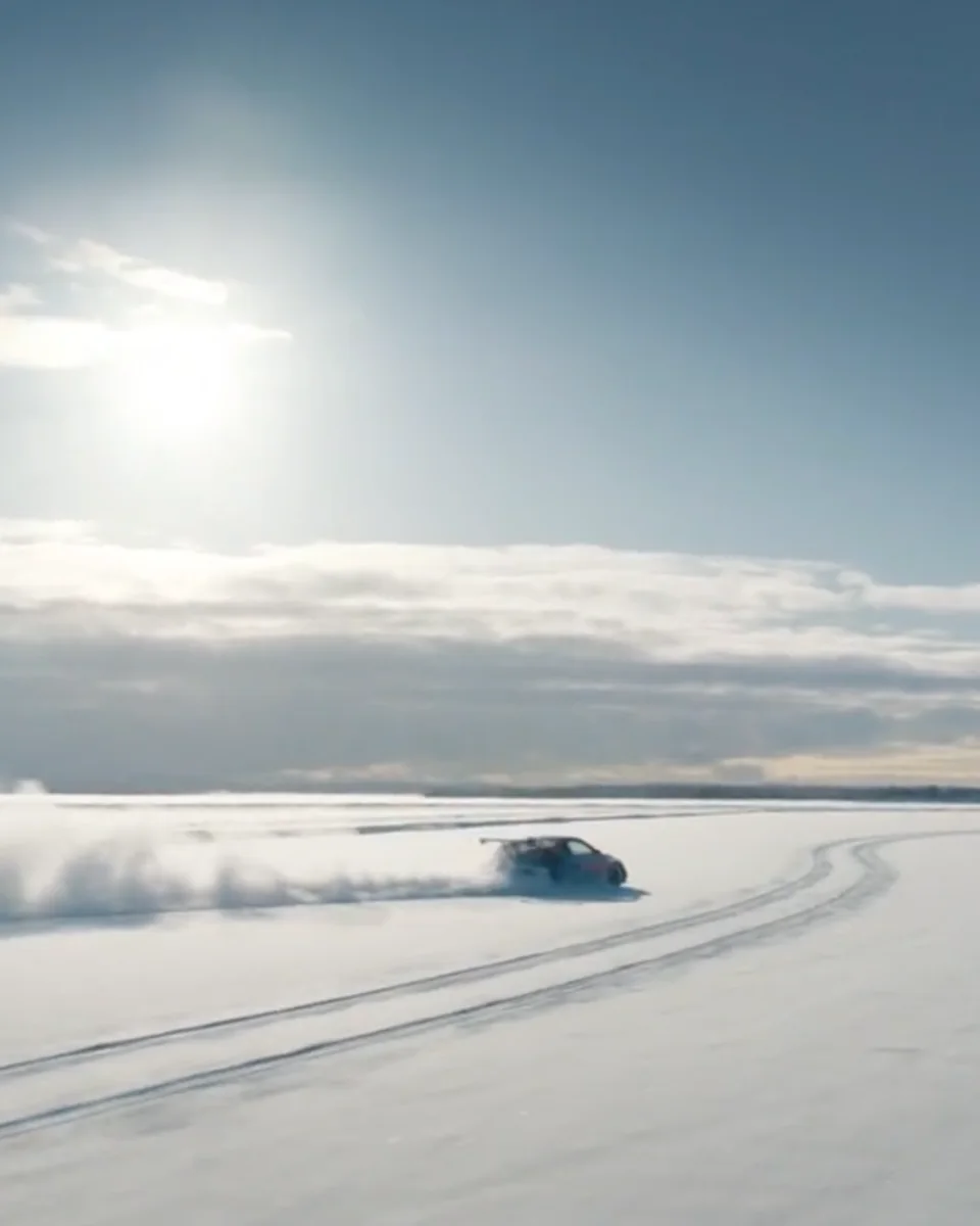 A car drifting across a frozen lake in low sun, snow spraying behind it
