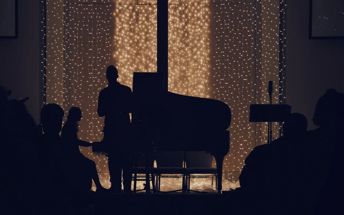 A pianist and a small audience in silhouette against a wall of lights