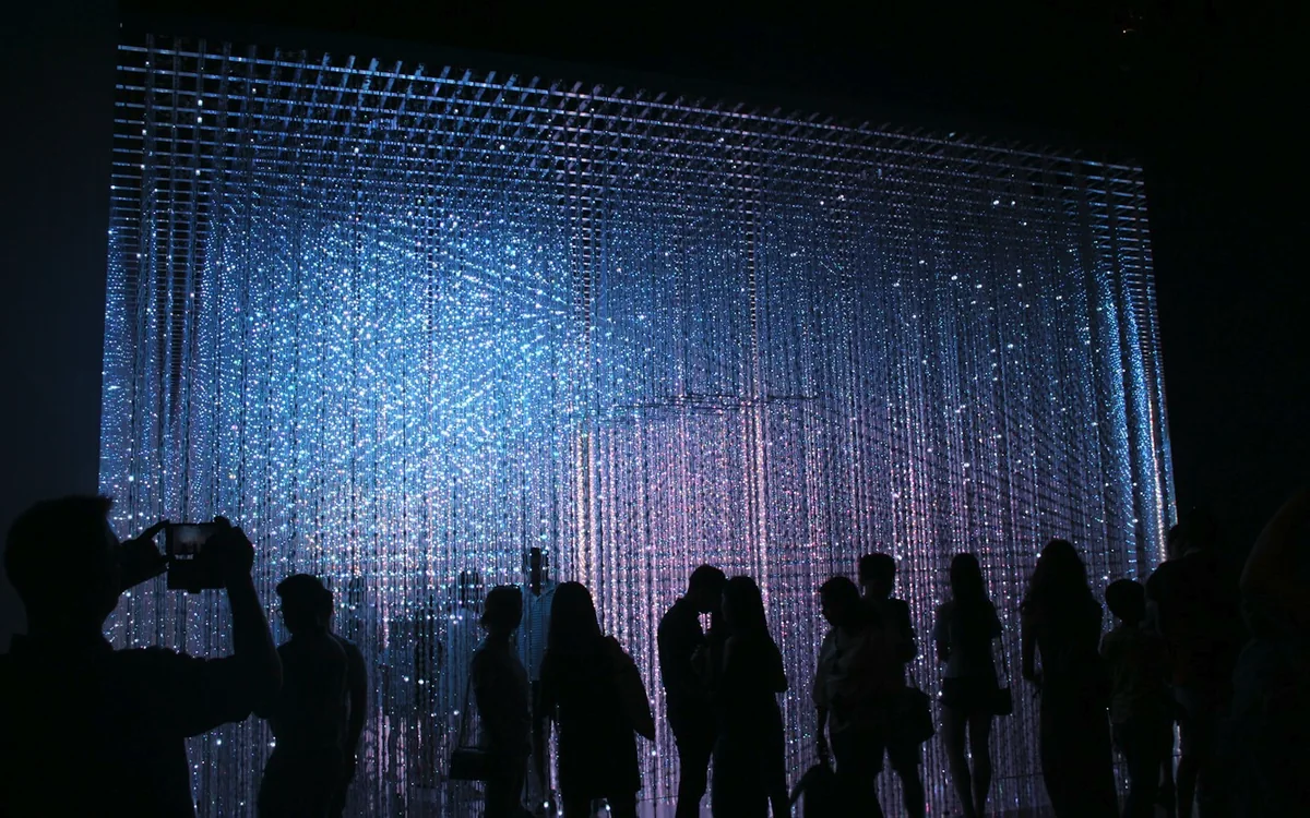 Guests in silhouette in front of a wall of light in a dark room